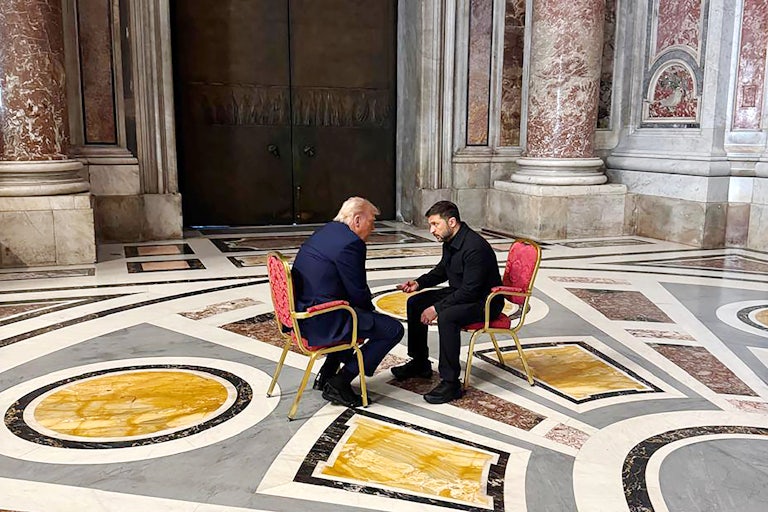 Ukraine's President Volodymyr Zelenskiy meets with Donald Trump. They are both seated on two chairs facing each other in the middle of an empty room at St. Peters Basilica.