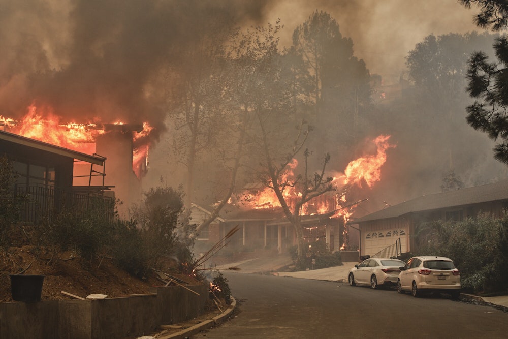Flames leap from roofs and smoke partially obscures a residential neighborhood with cars parked on the street.