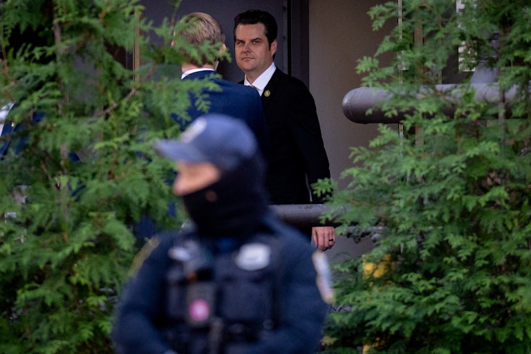 Matt Gaetz is seen walking between two trees, behind a security guard.