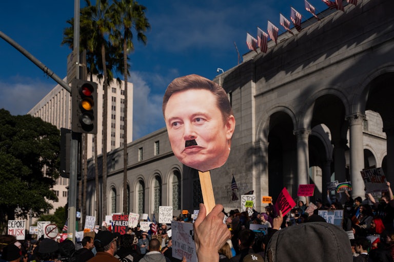 A protester holds up a sign of Elon Musk’s face with an Adolf Hitler mustache