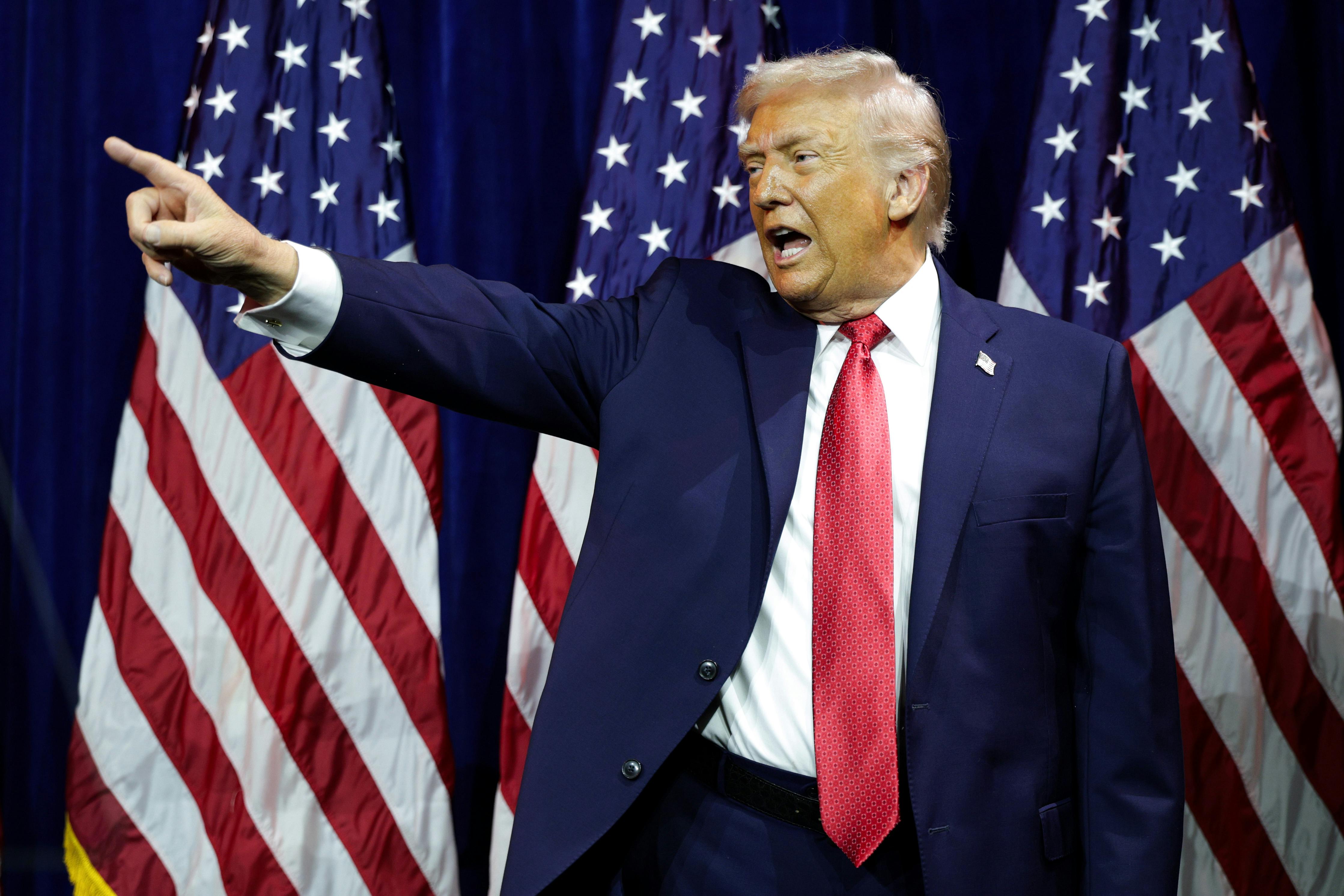 Donald Trump points while standing in front of U.S. flags.