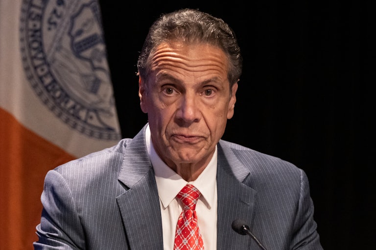 Andrew Cuomo presses his lips together while sitting in a press conference