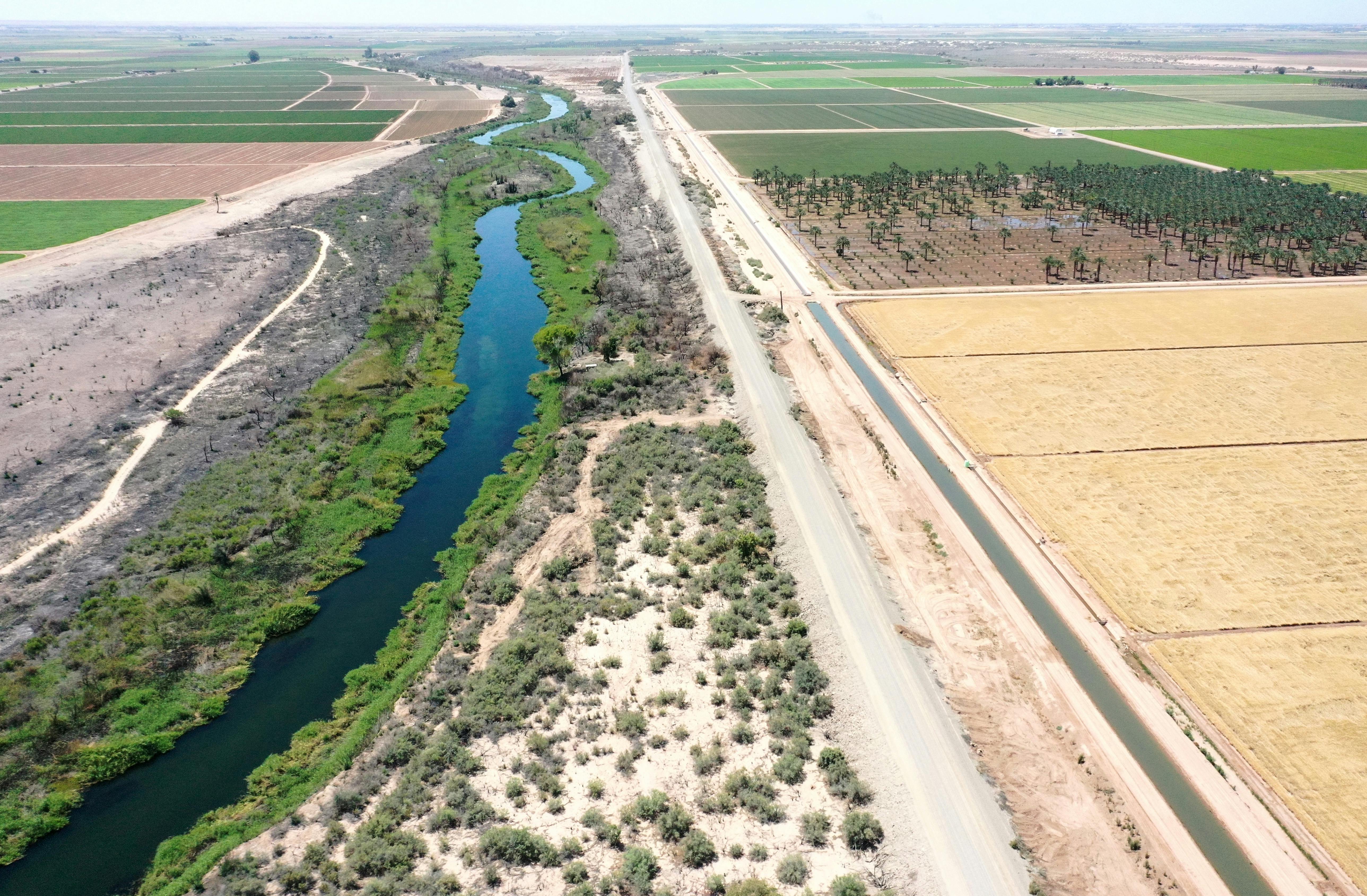 A river flows between farm fields, with green vegetation along its banks.