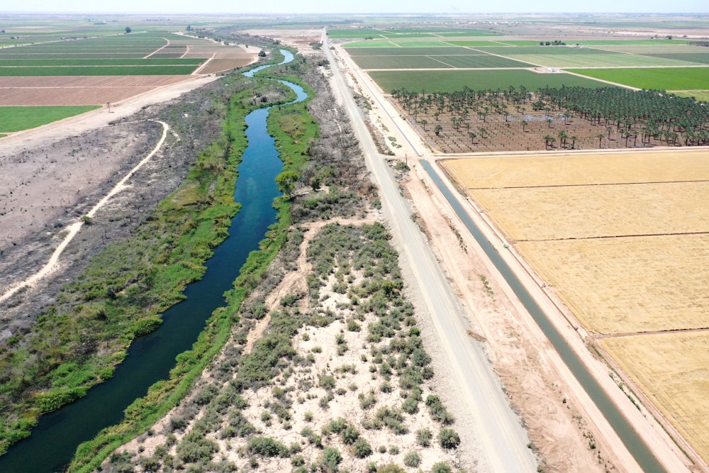 A river flows between farm fields, with green vegetation along its banks.