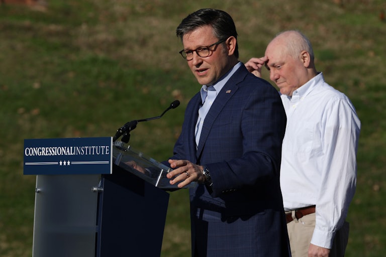 Mike Johnson speaks at a podium outside. Steve Scalise behind him holds his hand to his forehead.
