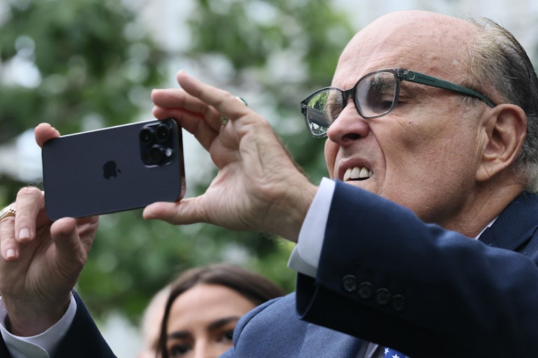 Rudy Giuliani squints and makes a weird face as he holds up his phone horizontally to take a photograph