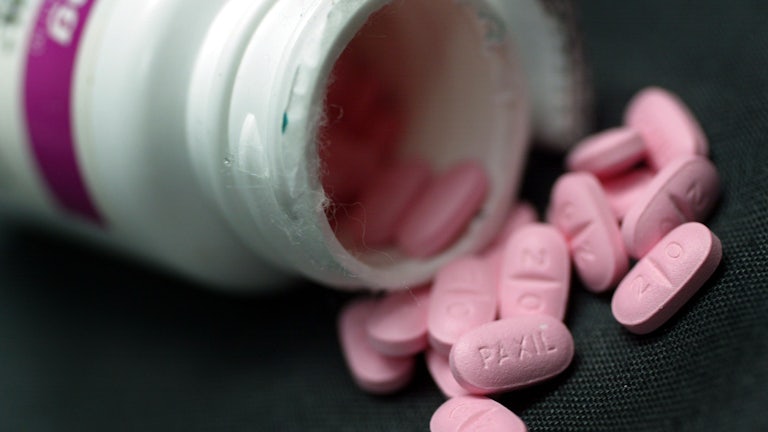 Pink pills spill out of an overturned bottle.