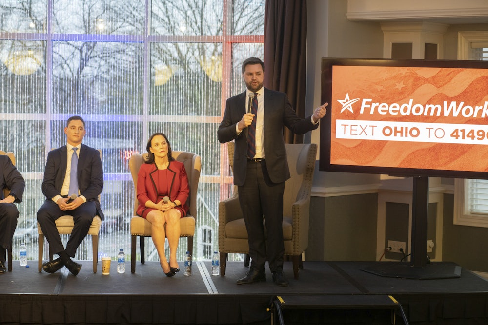 J.D. Vance stands on stage with two others in front of a screen reading "FreedomWorks."