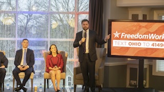 J.D. Vance stands on stage with two others in front of a screen reading "FreedomWorks."