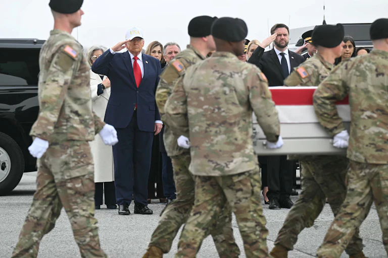 Donald Trump and JD Vance stand as military servicemembers escort the remains of fallen soldiers in front of them.