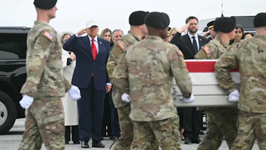 Donald Trump and JD Vance stand as military servicemembers escort the remains of fallen soldiers in front of them.