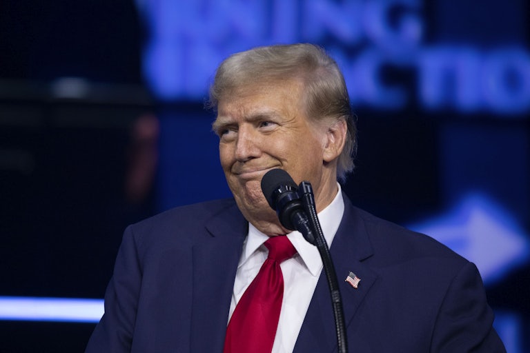 Donald Trump smiles weirdly at something off camera. A mic stands before him.