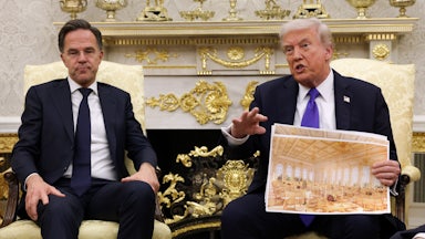 Trump holds an architectural rendering in front of a man who seems exasperated