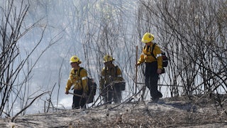 On July 6, three firefighters in yellow helmets walked through brush as they battled a wildfire in Montebello, California.