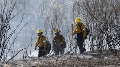 On July 6, three firefighters in yellow helmets walked through brush as they battled a wildfire in Montebello, California.