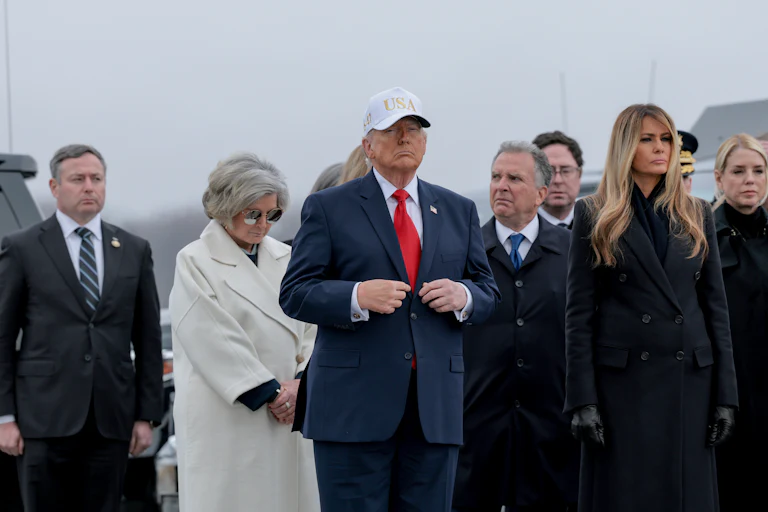 Donald Trump adjusts his suit while standing during a dignified transfer ceremony