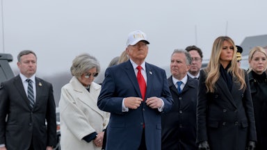 Donald Trump adjusts his suit while standing during a dignified transfer ceremony