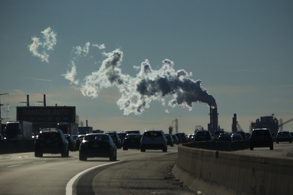 Cars move along a highway with a smokestack in the background.