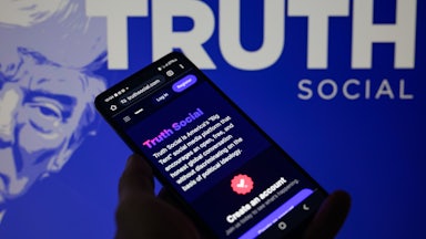 The Truth Social app is being displayed on a smartphone with Truth Social visible in the background in this photo illustration.