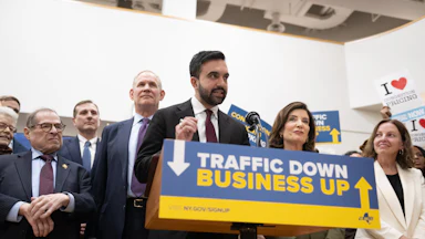 Zohran Mamdani, Kathy Hochul, and several others stand behind a podium reaching "Traffic Down. Business Up."