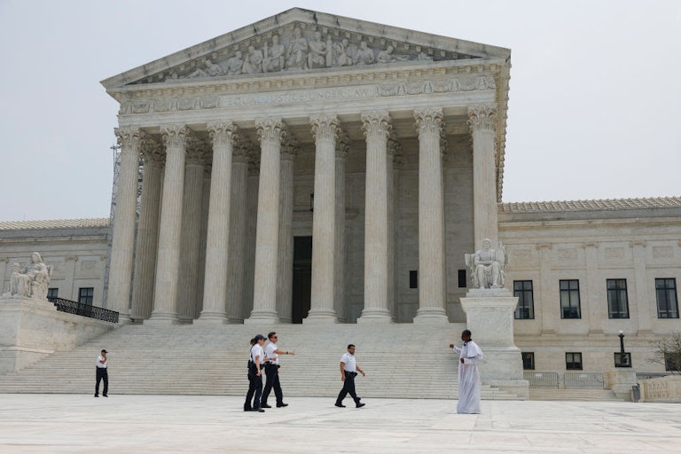 A photo of the front of the Supreme Court building with a few people walking by the steps. 