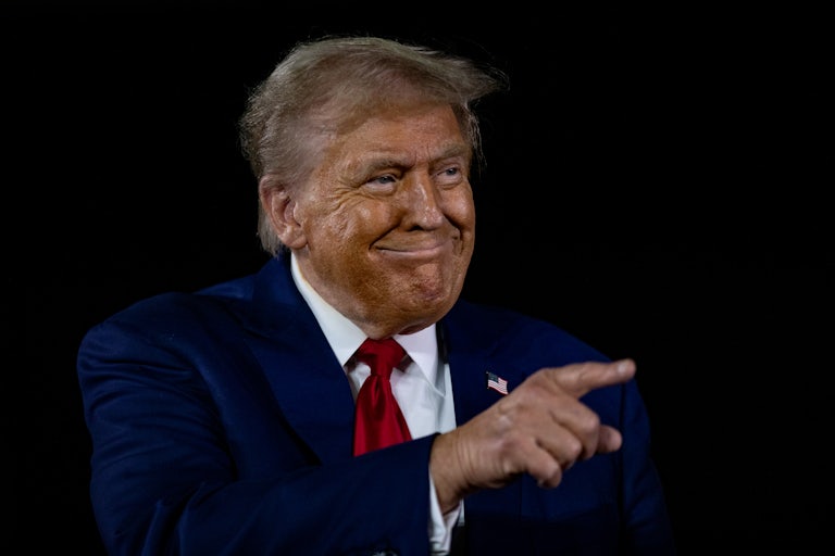 Donald Trump smiles weirdly and points at something or someone off screen