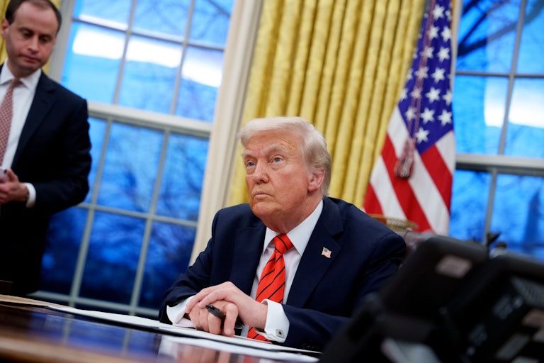 Donald Trump sits at his desk in the Oval Office. White House staff secretary Will Schar stands nearby.