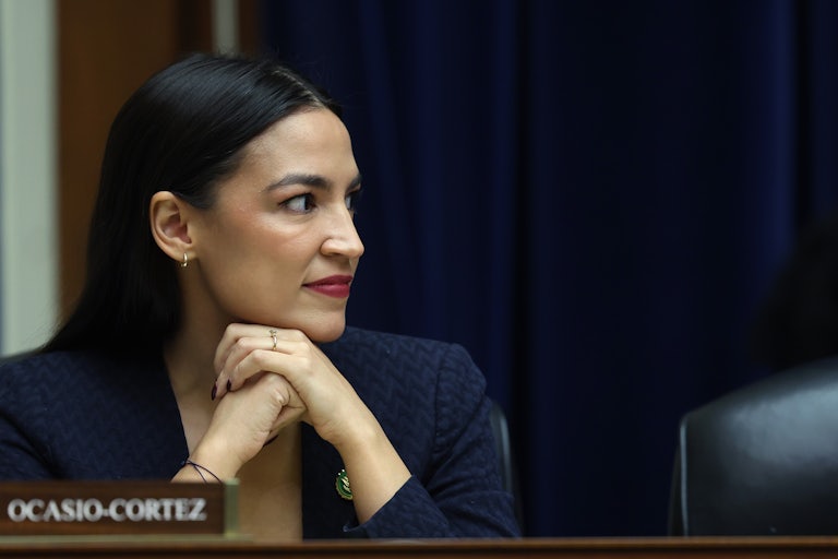 Representative Alexnadria Ocasio-Cortez rests her chin on her hands and smiles