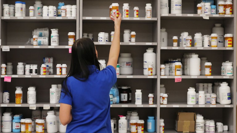 A woman takes a bottle off the top shelf of medications in a pharmacy