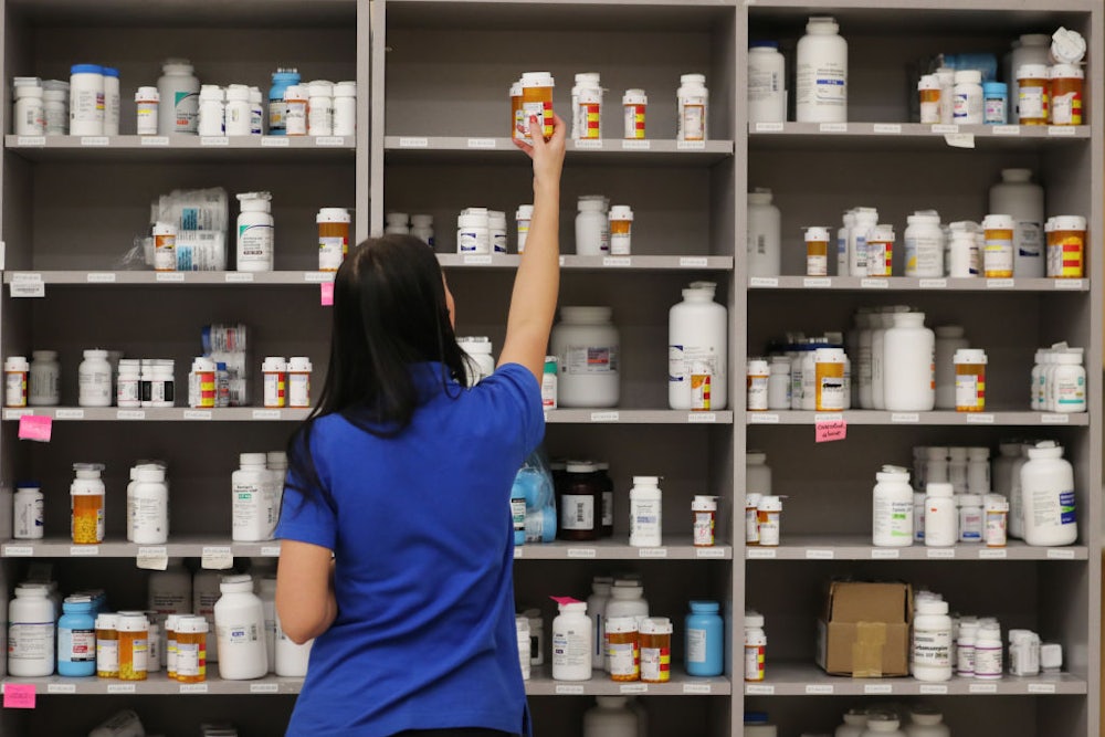 A woman takes a bottle off the top shelf of medications in a pharmacy