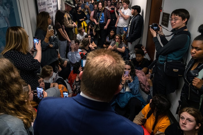 Crowded hallway packed with students (sitting, standing) looking at Representative Lamberth. The students hold phones and cameras documenting.