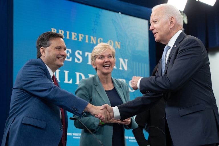 Joe Biden shakes hands with Ron Klain, standing in front of Jennifer Granholm.