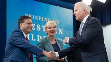 Joe Biden shakes hands with Ron Klain, standing in front of Jennifer Granholm.