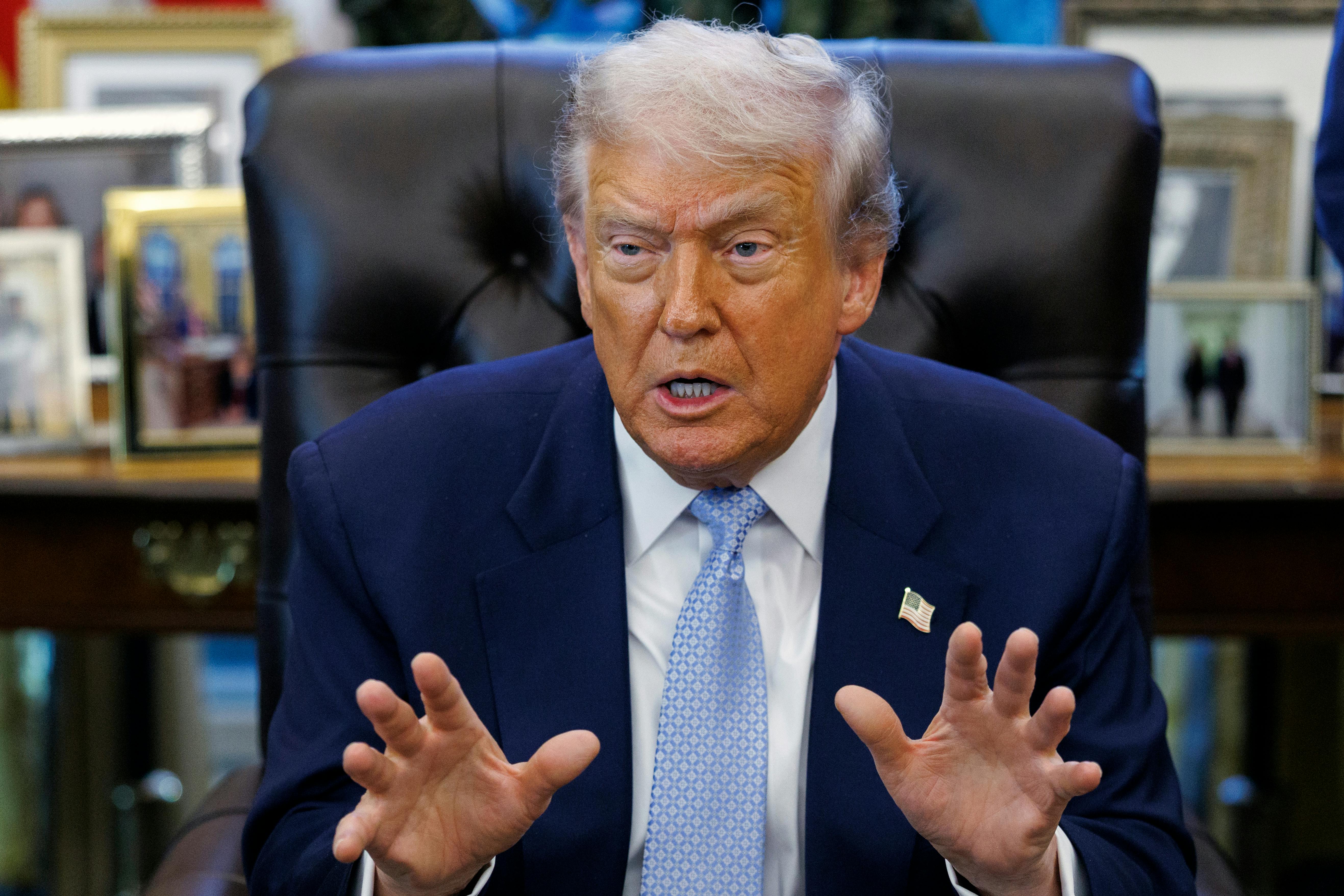 Donald Trump gestures and speaks while sitting at his desk in the Oval Office