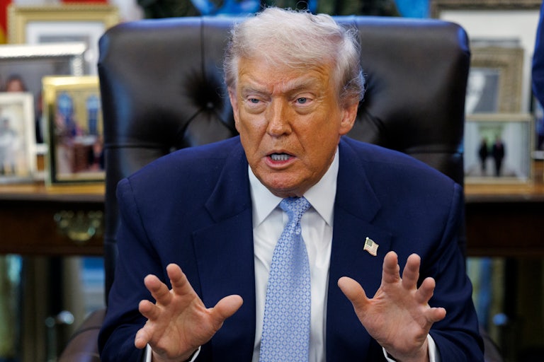 Donald Trump gestures and speaks while sitting at his desk in the Oval Office