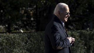 President Biden walks with shrubbery in the background.