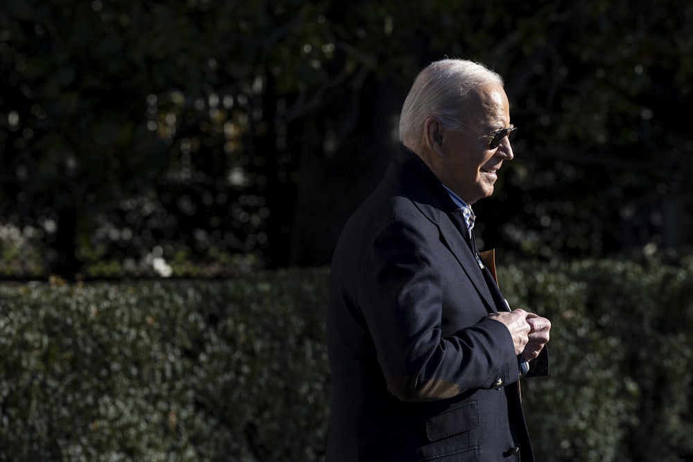President Biden walks with shrubbery in the background.