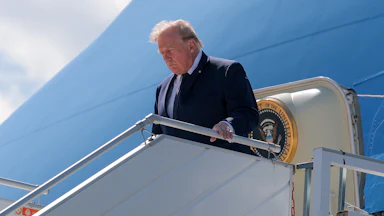 Donald Trump looks down and holds the railing while disembarking from Air Force One