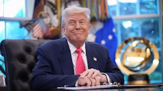 Donald Trump smiles while sitting at his desk in the Oval Office