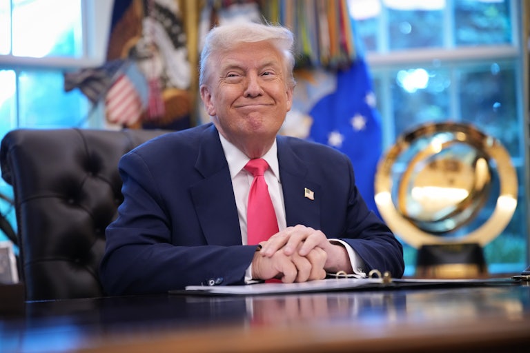 Donald Trump smiles while sitting at his desk in the Oval Office