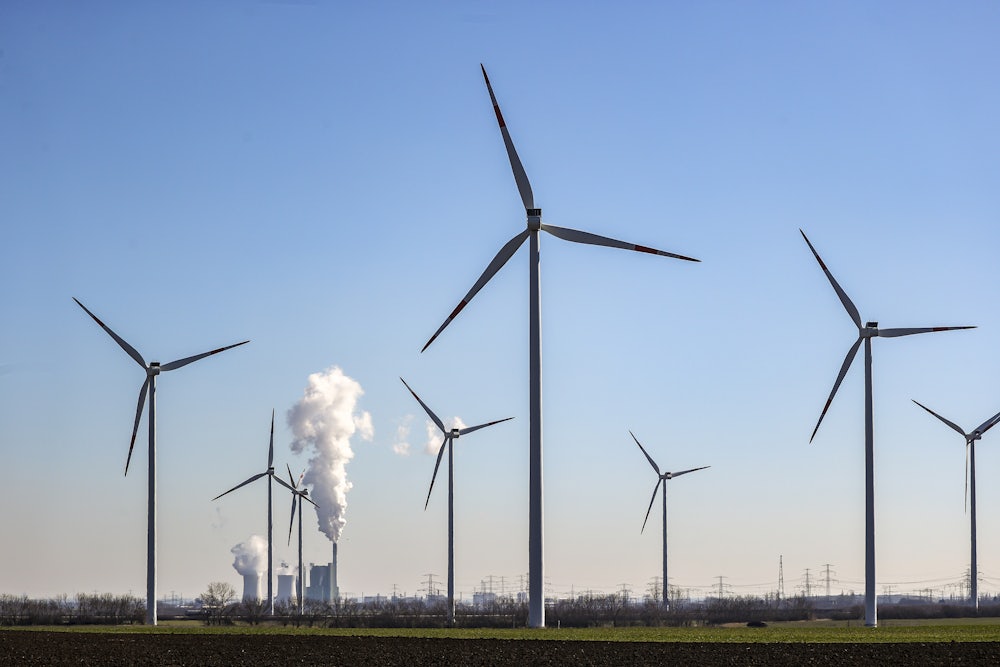 Coal plant towers steam behind wind turbines in the foreground.