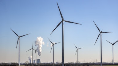 Coal plant towers steam behind wind turbines in the foreground.