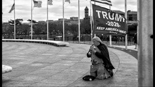 A man in a Revolutionary War costume kneels on the ground, clutching a Trump banner.