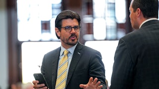 Texas state Representative Cole Hefner speaks while standing in the state Capitol. He holds a cell phone in one hand and gestures with the other