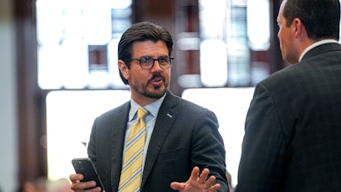 Texas state Representative Cole Hefner speaks while standing in the state Capitol. He holds a cell phone in one hand and gestures with the other