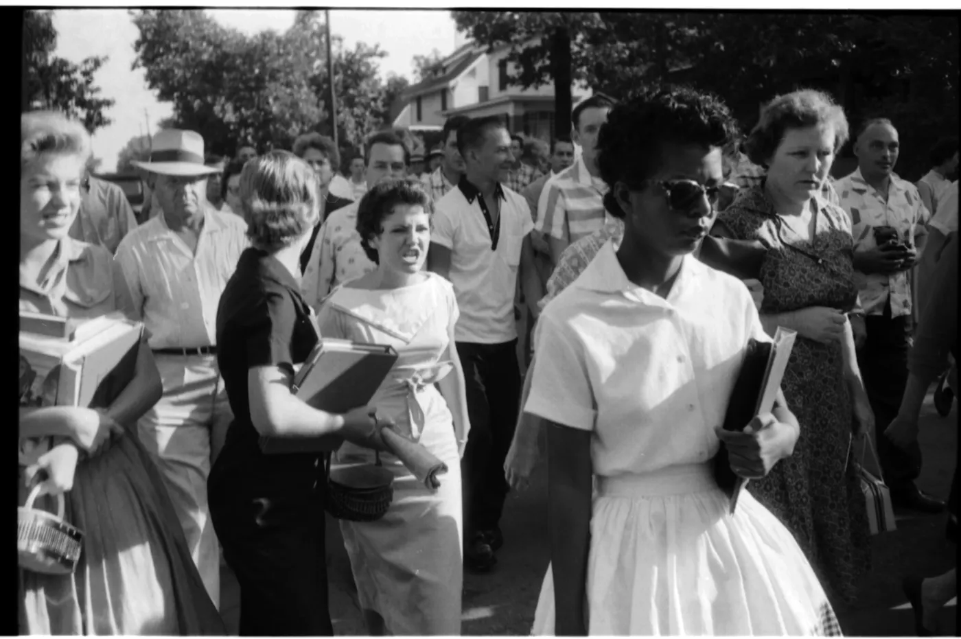 Elizabeth Eckford, wearing a white dress,  walks calmly carrying her schoolbooks while a hostile crowd of white students including Hazel Bryan jeer at her outside Central High School in Little Rock, Arkansas, September 4, 1957.