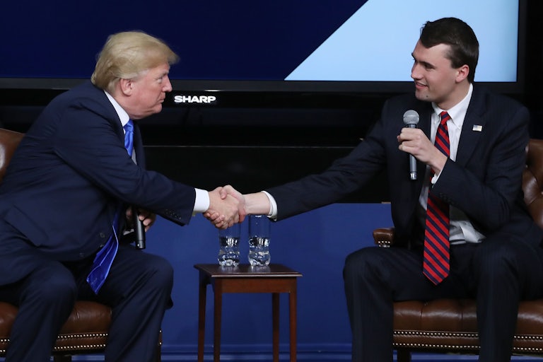Donald Trump and Charlie Kirk, both seated, shake hands. Kirk holds a mic in his hand.