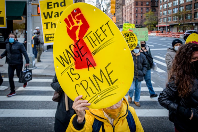 A New York City laundromat worker hold up a yellow sign that says "Wage Theft Is a Crime" during a protest in November 2020.