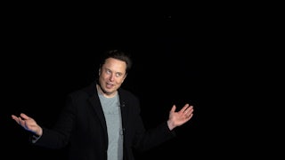 Elon Musk holds out his arms in front of a black background