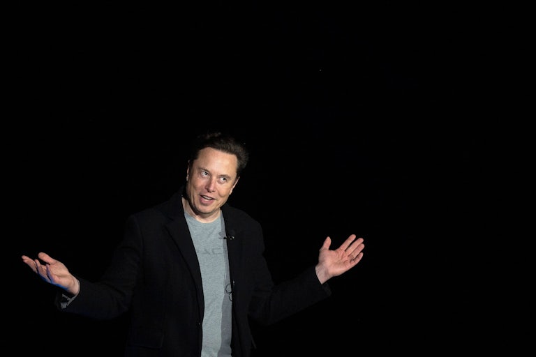Elon Musk holds out his arms in front of a black background
